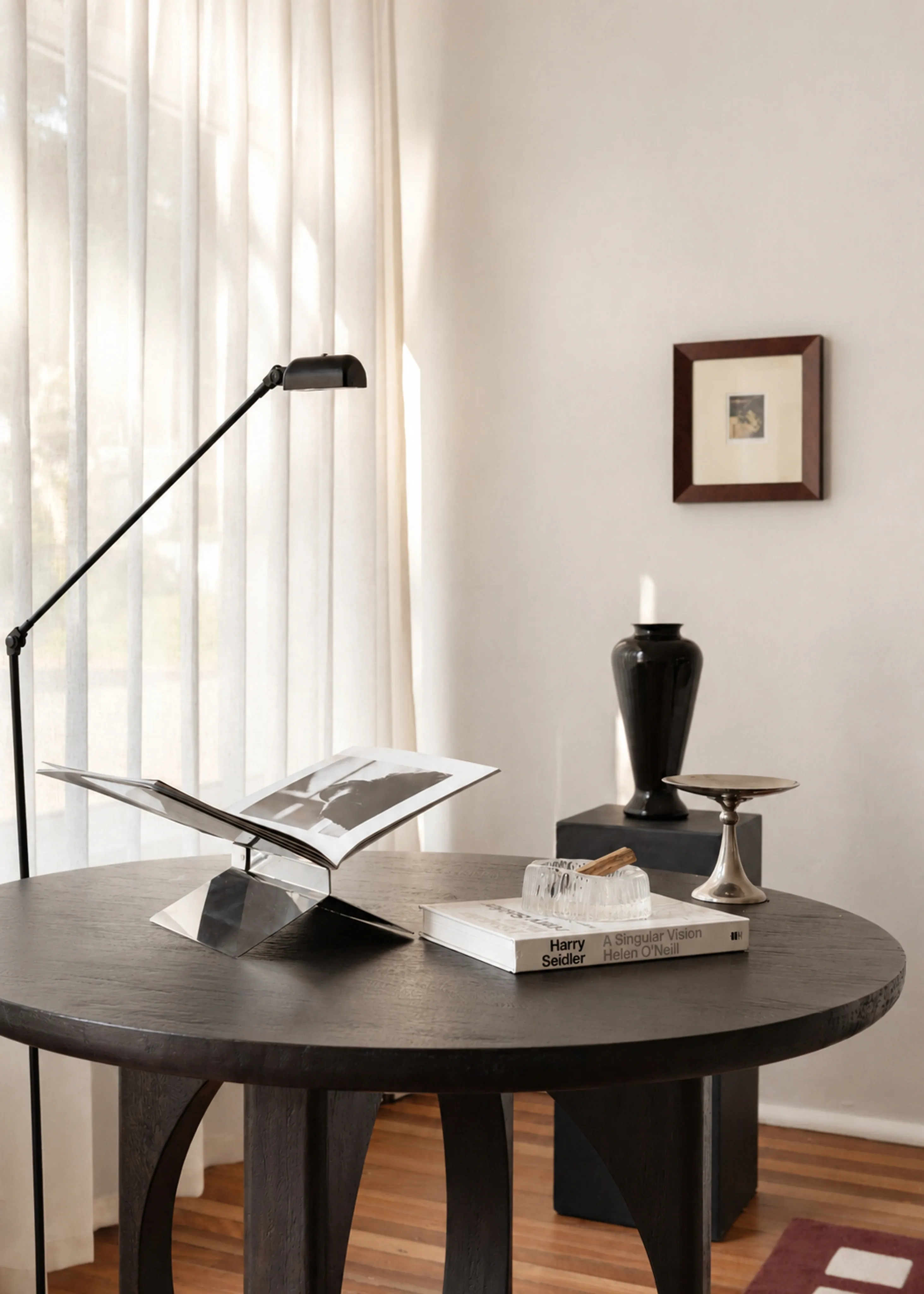 An open book, reading lamp and collected objects on a round table